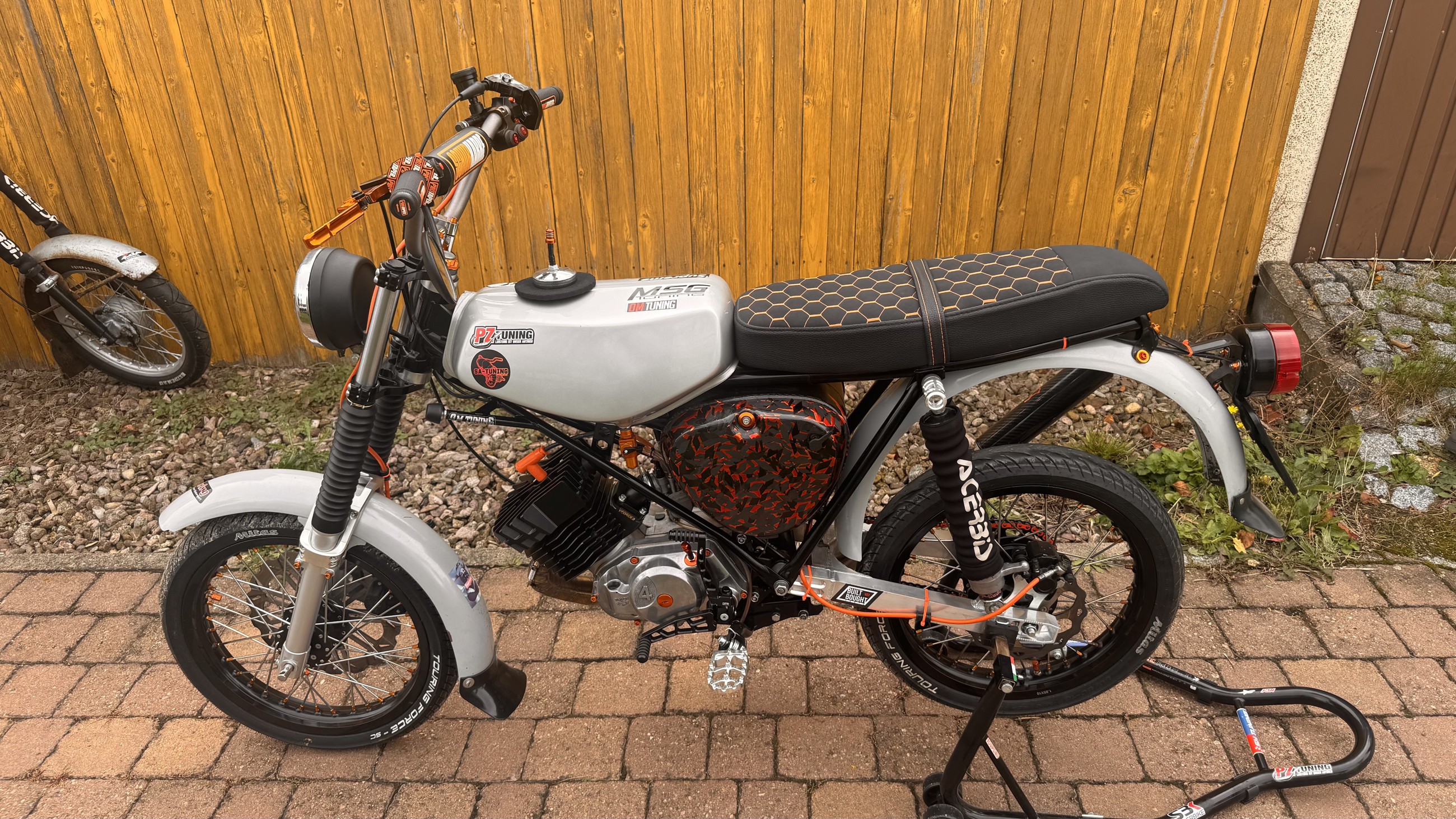 Tuning-Moped mit silbernem Tank, schwarzer Sitzbank und orangefarbenen Details